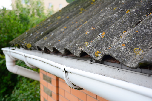 House asbestos roof with close up on gutter holder and plastic roof gutter pipe. Guttering.