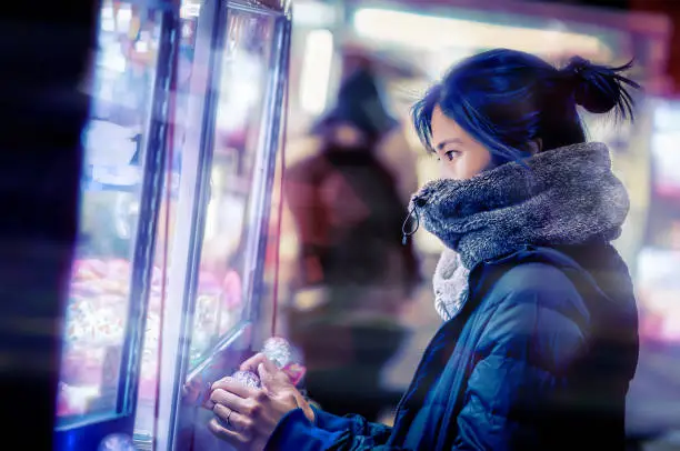 Photo of Japanese girl gamer in winter fashion is playing with crane doll machine in Game center for luck.