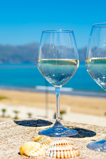 Two wine glasses with white wine served on outdoor terrace witn blue sea and mountains view on background in sunny summer day