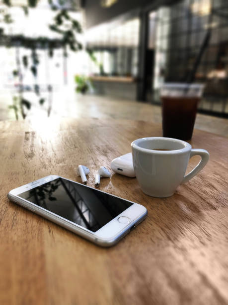 Izmir, Turkey - July  11, 2019: White colored Apple brand Iphone 8 Phone and Airpods 2 on a wooden table with charging box and cup of espresso on a wooden table.