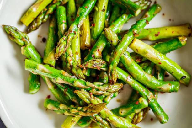 istock Cooked green asparagus with pepper and salt in a white bowl, top view. 1208413128