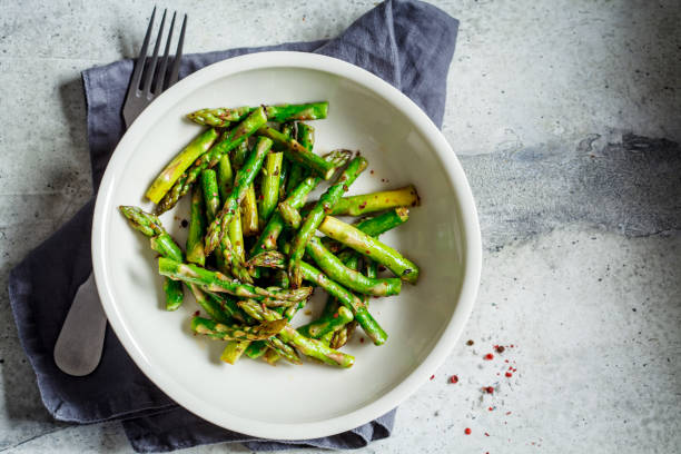 istock Cooked green asparagus with pepper and salt in a white bowl, top view. 1208413151