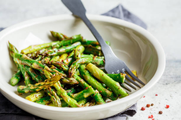 istock Cooked green asparagus with pepper and salt in a white bowl. 1208413172