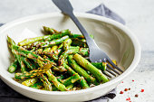 Cooked green asparagus with pepper and salt in a white bowl.