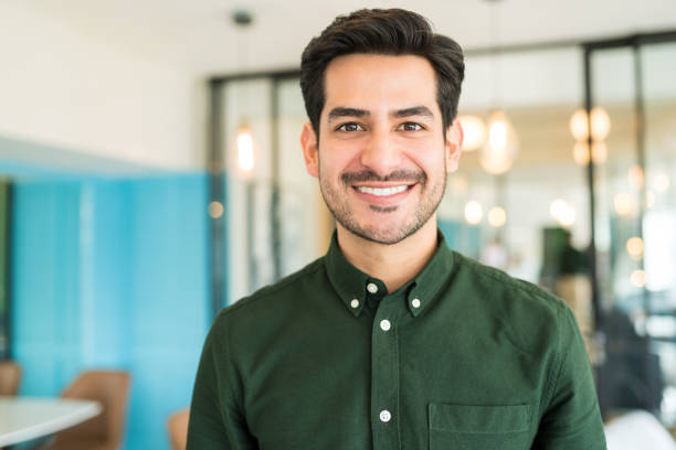 Happy Male Executive In Office Portrait of smiling Latin businessman standing at office headshot stock pictures, royalty-free photos & images