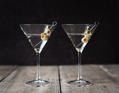 Two classic martini cocktails on wood table with black background.