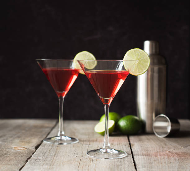Cosmopolitan martini drinks, shaker and limes on a wooden table.