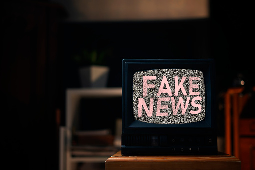 the old vintage tv with gray noise on screen with fake news text overlay, standing on shelf at home