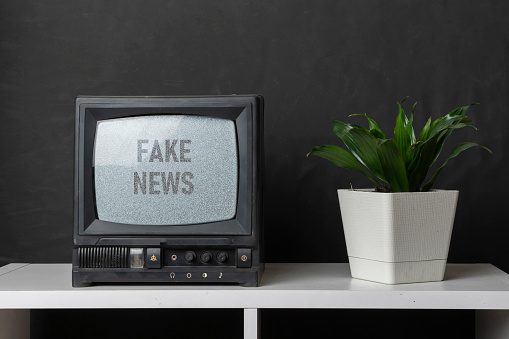 the old vintage tv with gray noise on screen with fake news text overlay, standing on shelf at home