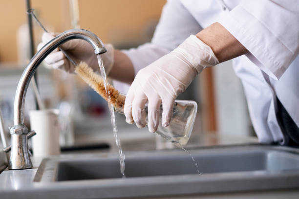 mains de personne dans des gants nettoyant et lavant des flacons de verre avec de l’eau dans le laboratoire - textile scientific experiment laboratory textile industry photos et images de collection