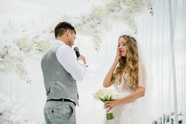 istock Happy bride and groom exchanging wedding vows on ceremony under the arch decorated with flowers and greenery on the backyard banquet area. The groom says the promise in the microphone. 1208417384