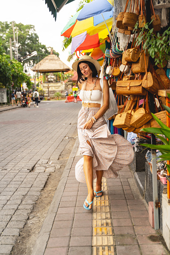 Cheerful girl in hat is spending hot day in street and walking near local souvenir market
