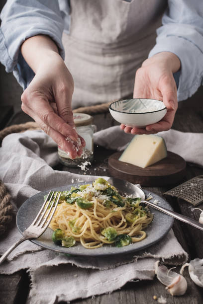 Chef hands cooking Italian pasta and adding cheese parmesan in dish on wooden table background. Chef serving homemade italian with brussels sprouts and cheese pasta on plate stock photo