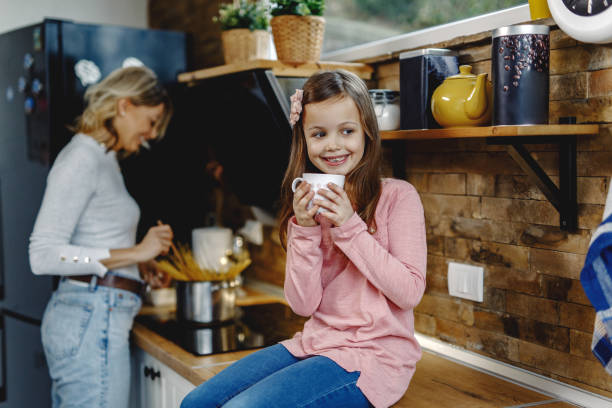 istock Cute small girl drinking tea while sitting on kitchen counter. 1208421532