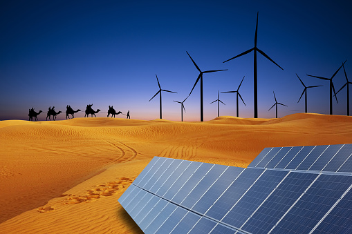 Renewable energy in desert sand dunes at sunset concept with solar panels and wind turbines