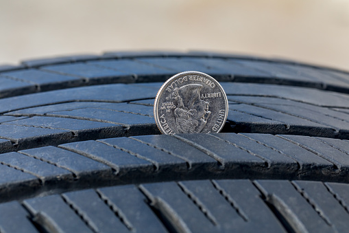 Primer plano de la comprobación de la profundidad de desgaste de la banda de rodadura de los neumáticos viejos con una moneda de cuarto. Concepto de seguridad, mantenimiento y reparación de automóviles photo