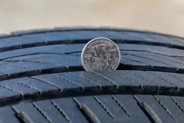 Photo of Closeup of checking tire tread wear depth of old tire using a quarter coin. Concept of automobile safety, maintenance, and repair