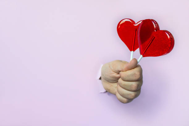 istock red lollipops on a heart shaped stick in your hand through a hole on a pink background 1208426962