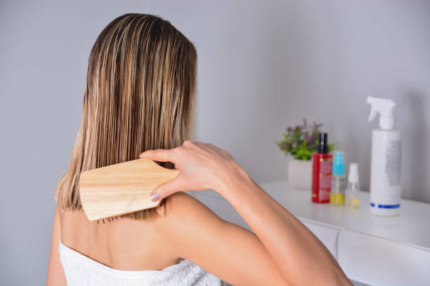 Woman with comb brushing her wet blonde hair after showering at home stock photo