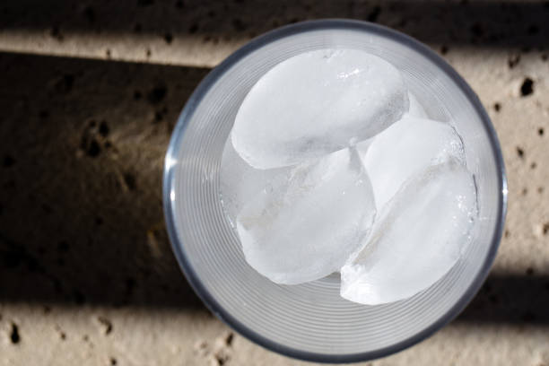 Ice cubes melting in a clear glass on a concrete deck, from above with shadows