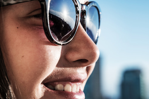 close-up portrait of young girl's face in sunglasses with cheerful smile, city background