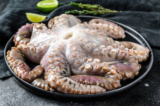istock Raw octopus in a plate with cooking ingredients. Black background. Top view 1208431694