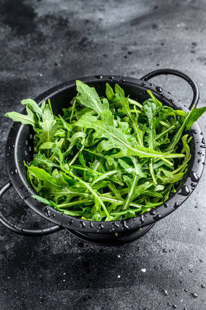 istock Fresh arugula leaves in a colander. Black background. Top view 1208434456