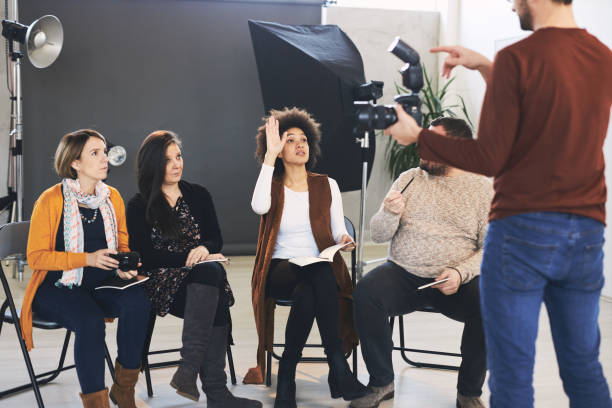 istock Group of happy attendees sitting and listening their tutor who holding camera and explaining them basics. 1208435710
