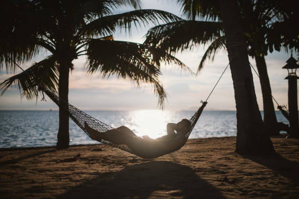istock A young man is lying in a hammock at sunset by the ocean. Handsome guy is resting in a hammock among palm trees on the seashore. 1208438171