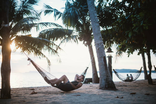 istock A young man is lying in a hammock at sunset by the ocean. Handsome guy is resting in a hammock among palm trees on the seashore. 1208438267