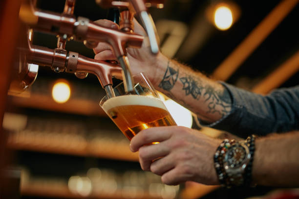 istock Tattooed caucasian barman pouring beer while standing in pub. Selective focus on hand. 1208445318