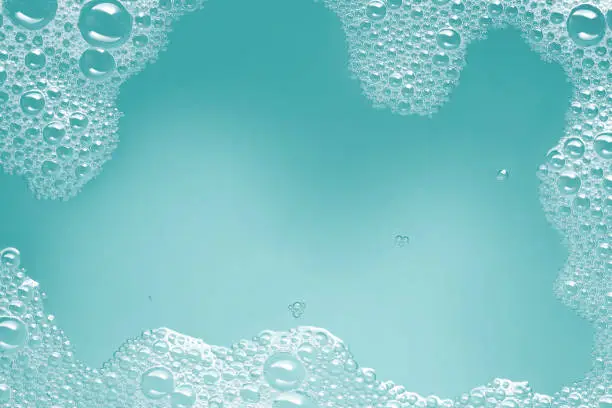 Close-up of soap suds with water on a turquoise blue background. Space for copy.