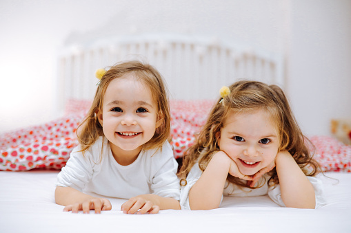 Cute sisters playing together in parent's bed, little girl looking at camera