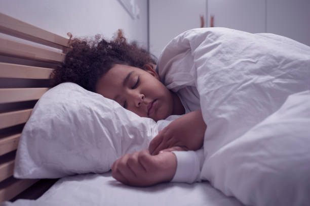 istock A child with a head-on white pillow and eyes closed sleeping in bed. 1208452978