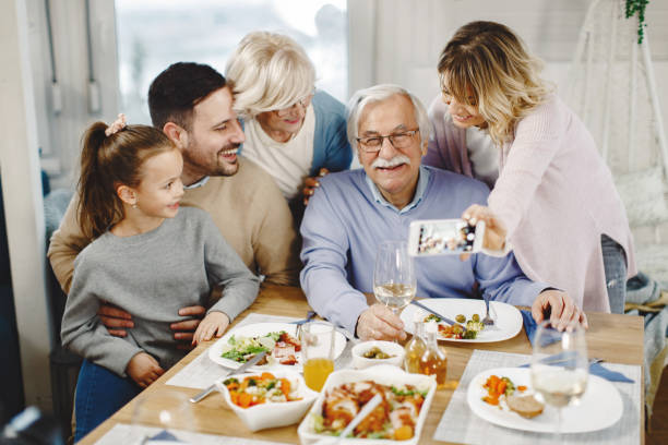 felice famiglia allargata che si diverte mentre si scatta selfie con lo smartphone nella sala da pranzo. - riunione di famiglia foto e immagini stock