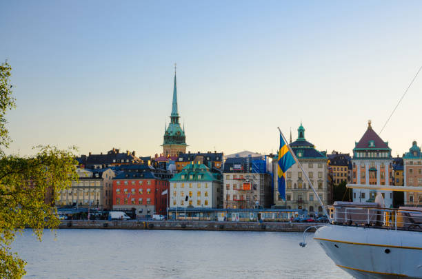 Old quarter Gamla Stan with traditional buildings, Stockholm, Sweden Old historical town quarter Gamla Stan with traditional typical buildings with colorful walls on Stadsholmen island and ship nose with sweden flag on water Lake Malaren at sunset, Stockholm, Sweden strommen stock pictures, royalty-free photos & images