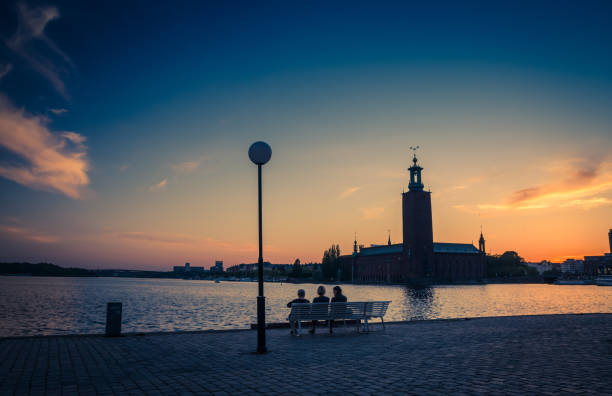 Silhouette of women sitting on bench, Stockholm City Hall, Sweden Silhouette of women sitting on bench at promenade quay bank of Lake Malaren looking at Stockholm City Hall Stadshuset tower building on Kungsholmen Island at sunset, dusk, twilight sky, Sweden kungsholmen town hall photos stock pictures, royalty-free photos & images