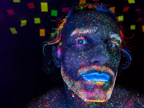 Glowing makeup on black background. Man with neon makeup powder on face, in studio