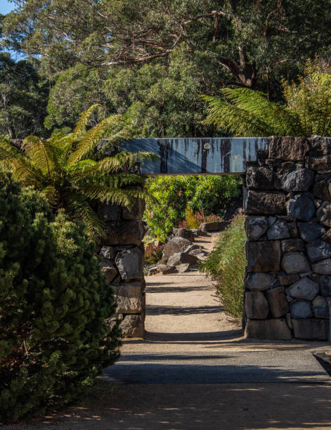 istock Garden path with rock feature wall, arch doorway along stone walkway surrounded by trees 1208475390