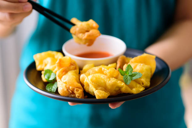 Deep-fried crispy wonton stuffed with minced pork, quail egg and shrimp eating with chili sauce by using chopsticks and holidng by hand, Asian food