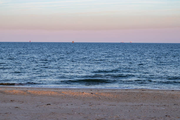 The sand on the beach and the water against the sunset on the horizon. A colorful sky at dusk along the beach at Fort Monroe in Hampton, Virginia. hampton virginia photos stock pictures, royalty-free photos & images