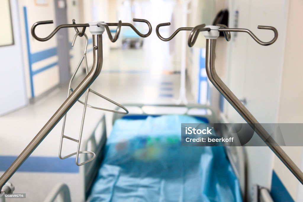 A vacant hospital bed in hallway with dropper stands. Hospital bed . A vacant hospital bed in hallway with dropper stands. Backgrounds Stock Photo