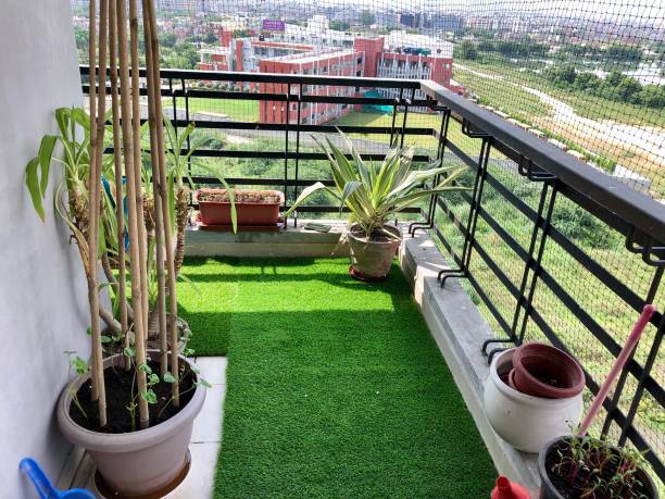 Image of residential balcony, Ghaziabad, India, designed with artificial grass turf and potted plants, pigeon anti-bird netting Stock photo of apartment balcony in Ghaziabad, India decorated with potted plants and artificial green grass turf. Gardening and exterior design concept. ARTIFICIAL GRASS stock pictures, royalty-free photos & images