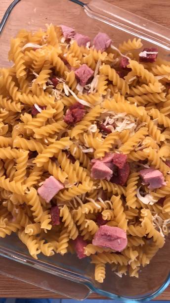 요리 파스타 굽기 조리법, 마른 파스타 트위스트, 다진 감몬 햄, 초리조 소시지 조각과 유리 오븐 접시에 강판 치즈의 이미지, 높은 전망 - dry pasta fusilli comfort food 뉴스 사진 이미지