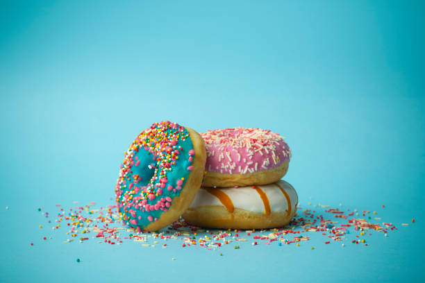 istock Donuts (doughnuts) of different colors on a blue background with multi-colored festive sugar sprinkles. Holiday and sweets, baking for children, sugar concept 1208507715