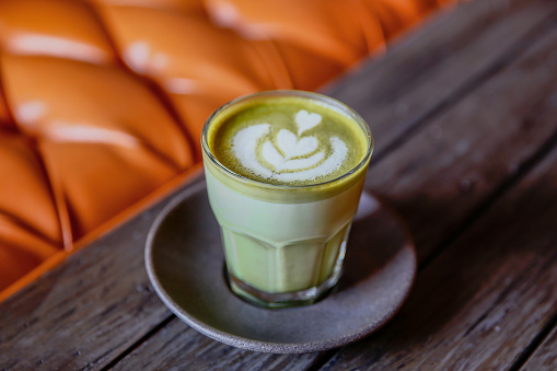 Close up shot of green tea latte with leaf shape froth art on wooden table