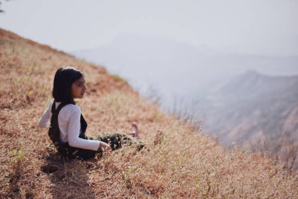 istock Girl (6-7 years) sitting in the grass looking at valley view 1208508773
