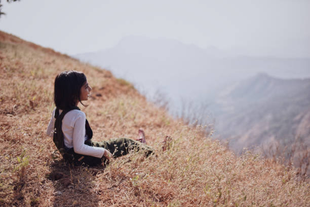 istock Girl (6-7 years) sitting in the grass looking at valley view 1208508798