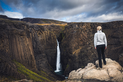 Young woman hiking toward Hengifoss waterfall (east Iceland).