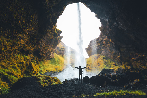 Woman with arms outstretched standing behind the waterfall in south of Iceland.